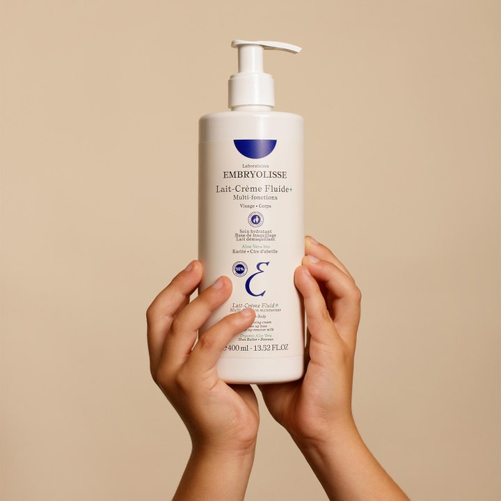 Embryolisse Lait-Crème Fluid+ 400 ml multifunktionell dagkräm för torr hud ansikte och kropp i vit pumpflaska i händer