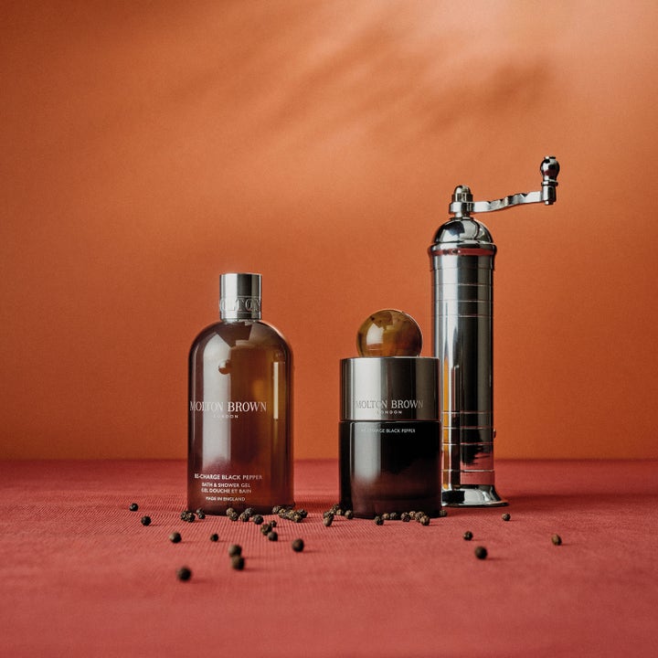Molton Brown Black Peppercorn Body Wash 300 ml aromatisk duschtvål med svartpeppar parfym bredvid en silverkvarn.