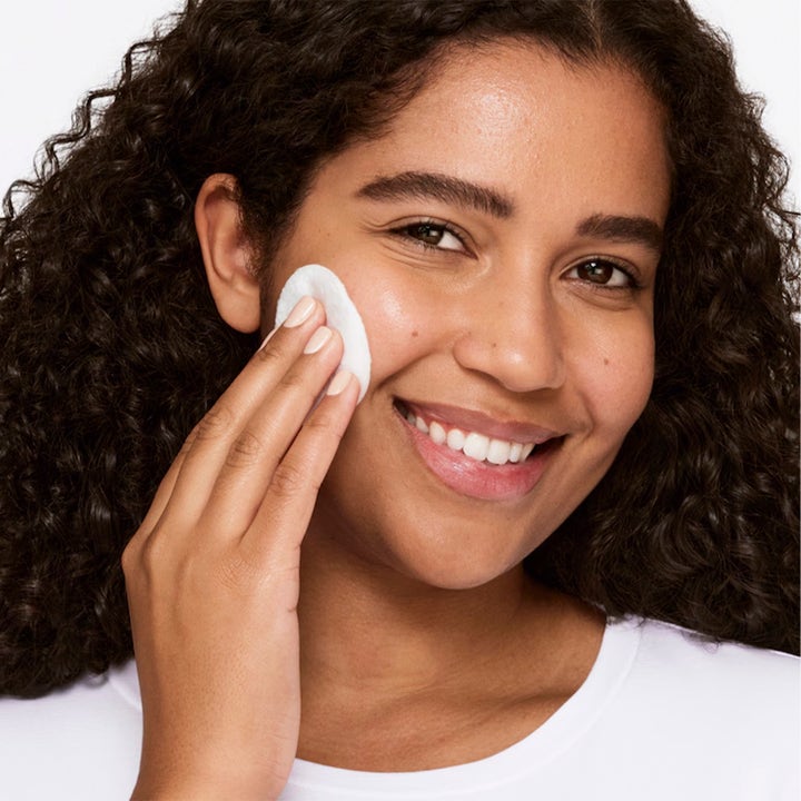 Clinique Clarifying Lotion 3 487 ml exfolierande ansiktsvatten som kvinna applicerar på kinden med bomullsrondell