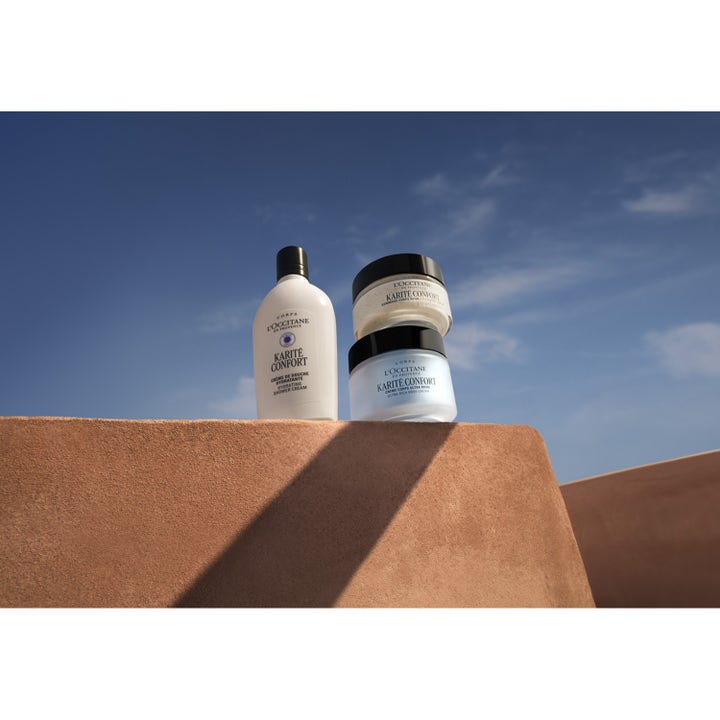 L'Occitane Shea Butter Rich Body Scrub 200 ml mjukgörande kroppsskrubb i burk med svart lock mot en klarblå himmel.