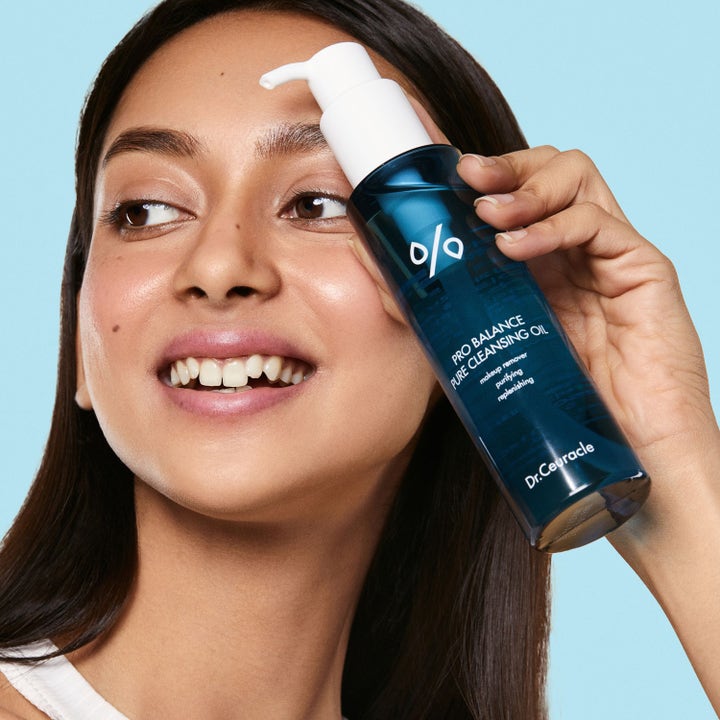 Dr. Ceuracle Pro Balance Pure Cleansing Oil 155 ml ansiktsrengöring i blå flaska hålls av en leende kvinna.