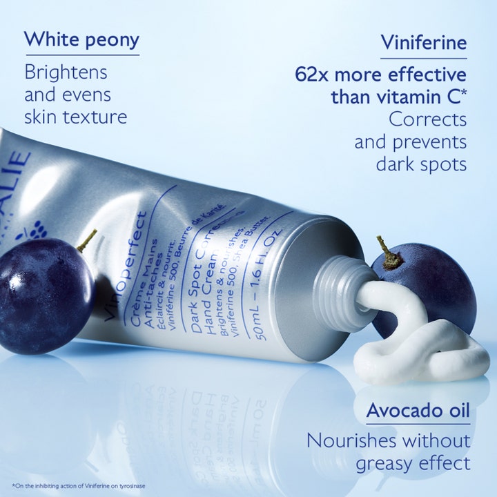 Caudalie Vinoperfect Hand Cream 50 ml mot mörka fläckar visar krämig vit textur ur silvertub intill blå vindruvor.