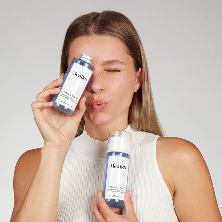 Medik8 Press & Clear 150 ml 2% BHA tonic hudvård i pumpflaska och refill som hålls upp av en kvinna