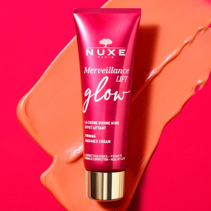 Nuxe Merveillance Lift Glow 50 ml anti-aging glow kräm i rödrosa tub placerad på en persikofärgad krämtextur.