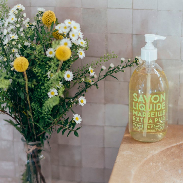 Compagnie de Provence Verbena 495 ml flytande handtvål från provence i klar pumpflaska bredvid vackra sommarblommor