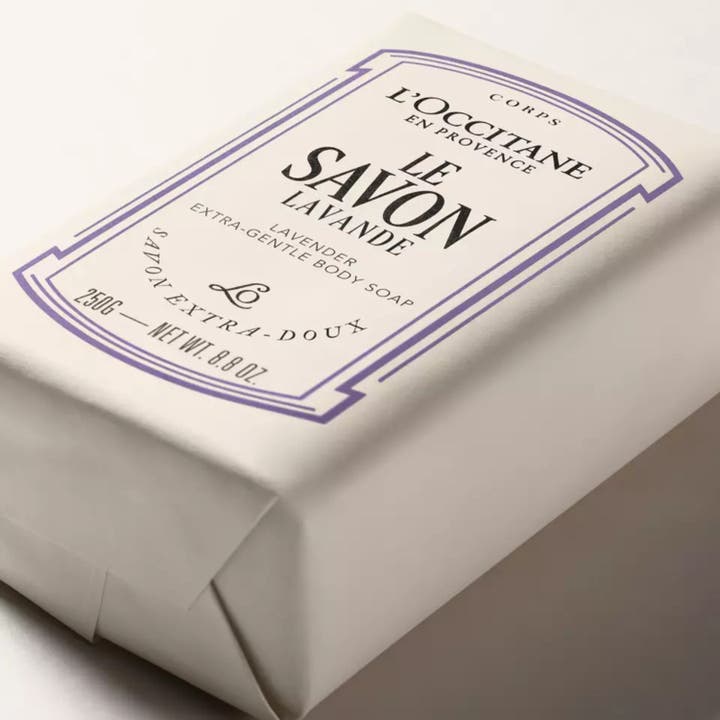 L'Occitane en Provence Extra Gentle Soap Lavender 250 g extra mild lavendeltvål i vitt pappersomslag med lila ram.