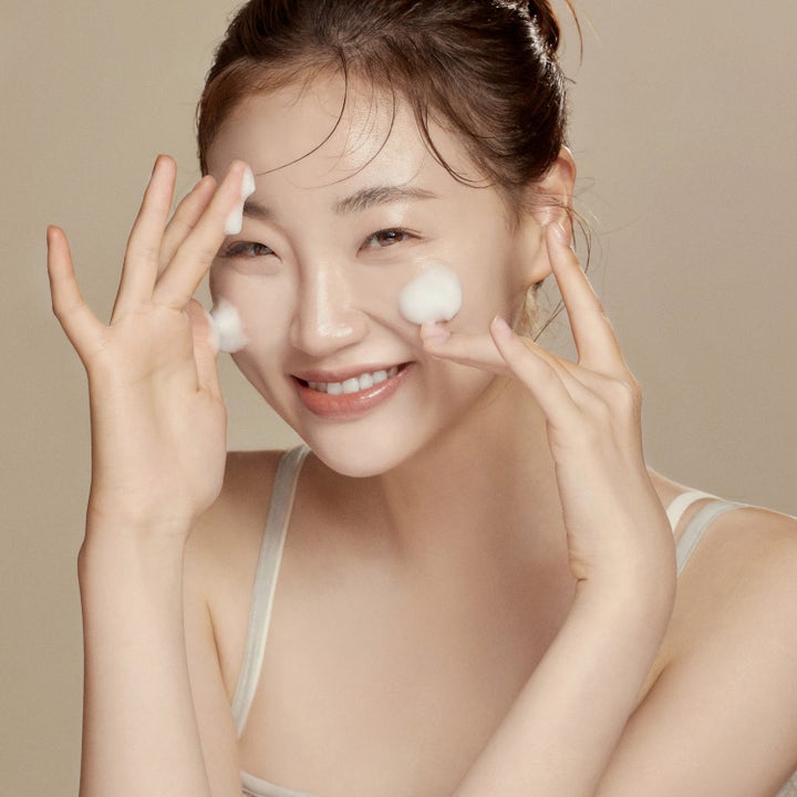 Hyggee All-In-One Care Cleansing Foam 150 ml rengöringsskum som en leende kvinna applicerar i ansiktet.