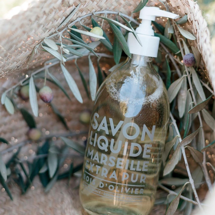 Compagnie de Provence Olive Wood 495 ml lyxig extra ren handtvål i glasflaska omgiven av färska olivkvistar.