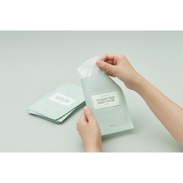 I'm from Vitamin Tree Sheet Mask 1 st lystergivande ansiktsmask händer drar ut en vit mask ur en ljusgrön sachet
