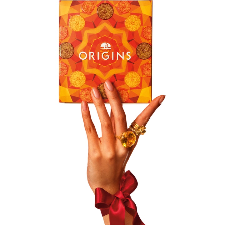 Origins Ginzing Glowing Essentials Set energiboostande hudvårdsset i orange citrusmönstrad box hållen av en hand.