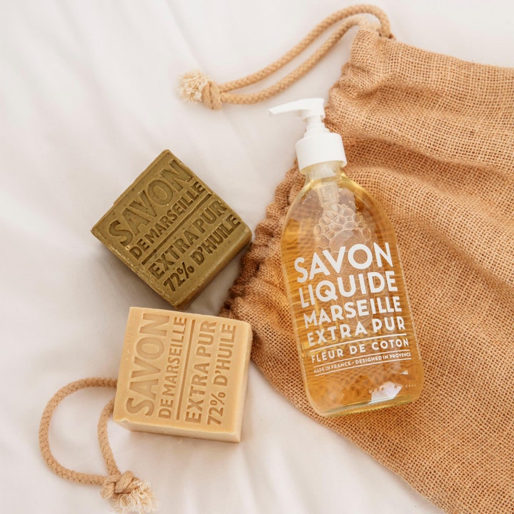 Compagnie de Provence Cube Of Marseille Soap Olive 400 g ekologisk olivtvål i blockform bredvid flytande tvål på tygpåse.