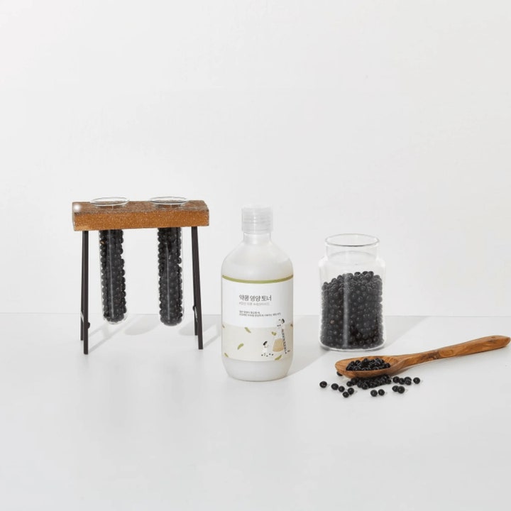 Round Lab Soybean Nourishing Toner 300 ml närande toner i vit flaska omgiven av svarta sojabönor och en träsked.