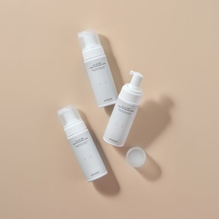 Hyggee All-In-One Care Cleansing Foam 150 ml rengöringsskum i vita pumpflaskor på en beige bakgrund.