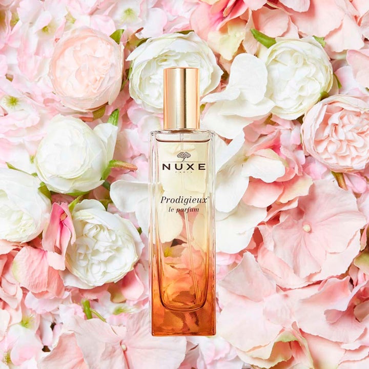Nuxe Prodigieux le parfum 50 ml parfym i elegant gradient glasflaska med guldlock på en bädd av rosa blommor.