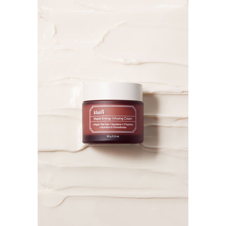 Klairs Maple Energy Infusing Cream 60 g lönn-infunderad ansiktskräm i brun burk mot en bakgrund av fyllig krämtextur.
