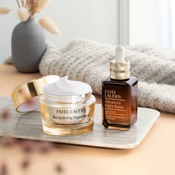 Estée Lauder Revitalizing Supreme + Soft Cream 30 ml dagkräm i öppen guldglasburk bredvid serum på en marmorbricka.