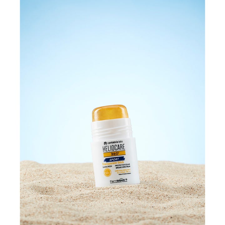 Heliocare Sport Stick SPF 50+ 25 g transparent heliocare solstift spf 50 i vit hylsa stående i sand mot blå himmel.