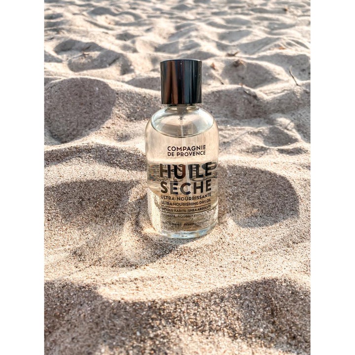 Compagnie de Provence Ultra Nourishing Dry Oil 100 ml närande kroppsolja i glasflaska på en solig sandstrand