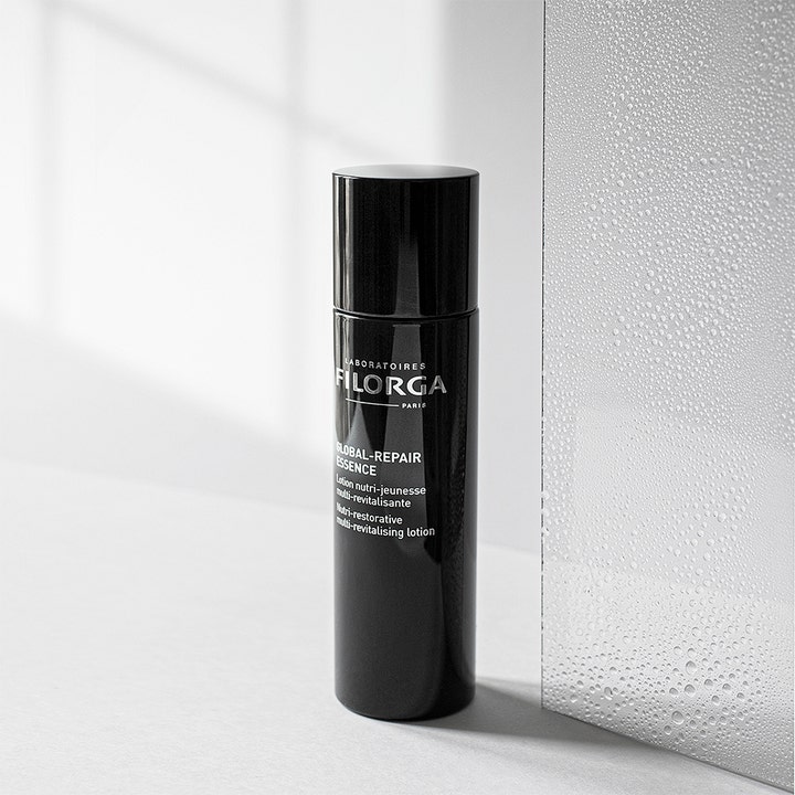 Filorga Global-Repair Essence 150 ml anti age essence behandling i en svart flaska bredvid en frostad glasskiva.