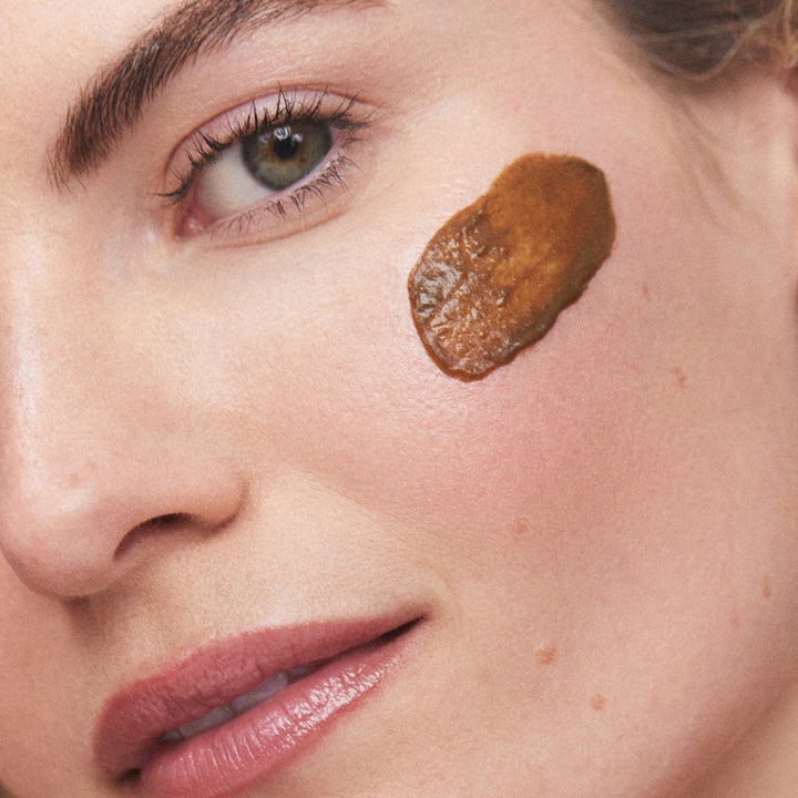 KORA Organics Turmeric Scrub & Mask 30 ml 2-i-1 exfoliering med brun kornig textur applicerad på en kind