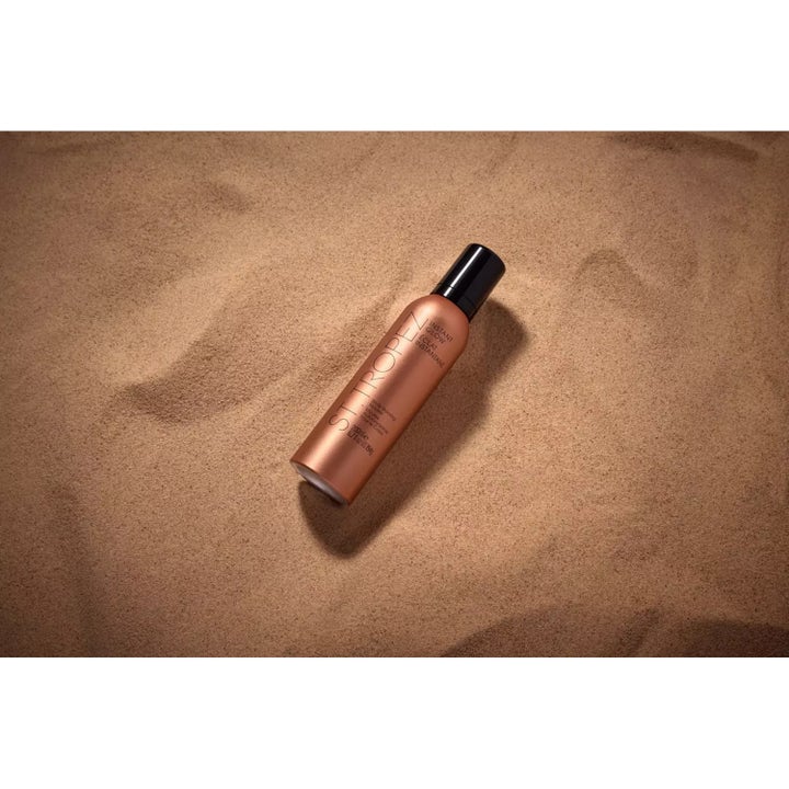 St.Tropez Instant Glow Body Bronzing Mousse 200 ml brun utan sol i bronsflaska placerad i finkornig sand ger lyster.