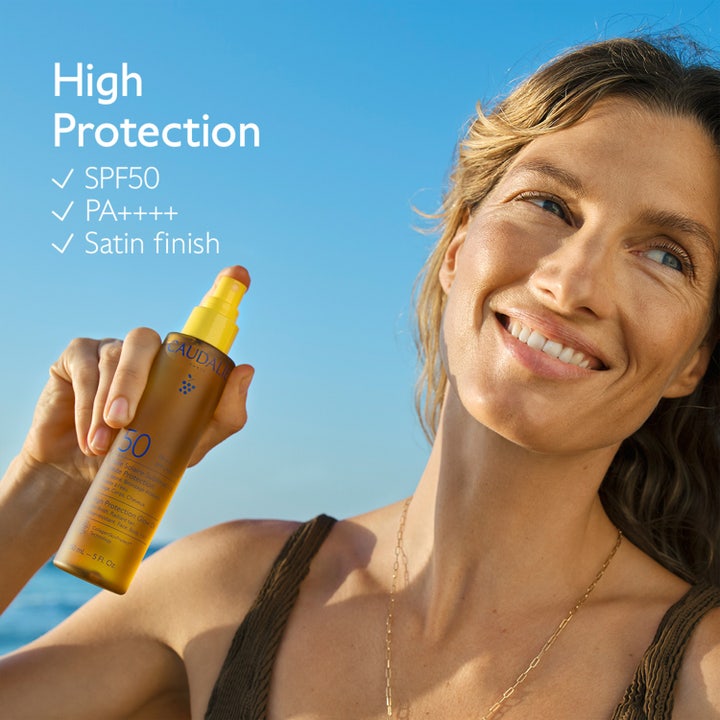 Caudalie Vinosun Glow Oil SPF50 150 ml ger lyster och skydd i en sprayflaska som hålls av en kvinna i solljus