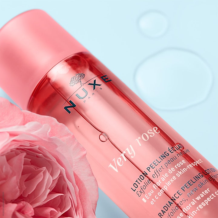 Nuxe Very Rose Peeling Lotion 150 ml kemisk peeling för strålande hy i rosa flaska bredvid en vacker ros