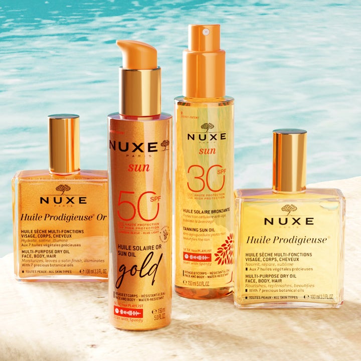 Nuxe Sun Tanning Oil Gold SPF50 150 ml lyxig sololja i pumpflaska framför glittrande blått vatten
