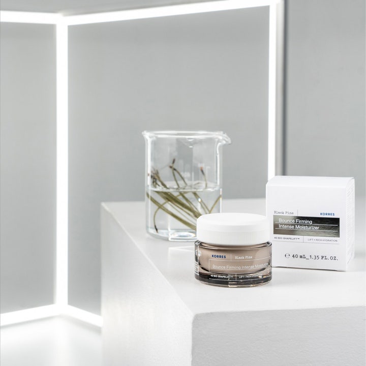 KORRES Black Pine 4D Bounce Firming Intense Moisturizer 40 ml 4d fuktkräm ansikte i glasburk bredvid bägare med tallkvistar