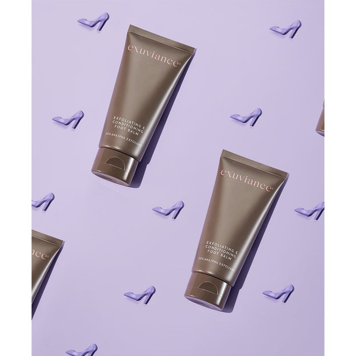 Exuviance Exfoliating & Conditioning Foot Balm 50 g AHA fotexfoliering i bruna tuber mot torr hud fötter på lila yta.