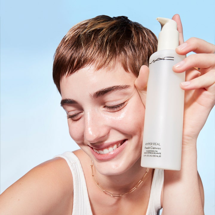 MAC Cosmetics Hyper Real Fresh Canvas Cleansing Oil 200 ml djuprengörande ansiktsolja i vit flaska som hålls av en modell