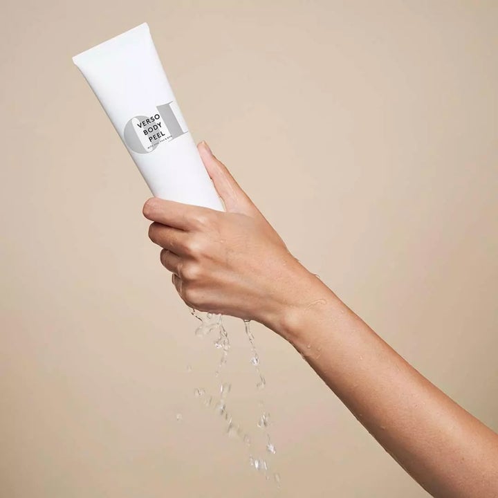 Verso N°10 Body Peel 150 ml exfolierande body scrub i vit tub som hålls i en hand med rinnande vatten