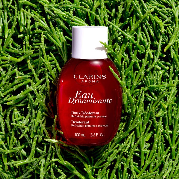 Clarins Eau Dynamisante Deodorant 100 ml uppfriskande deodorant i röd flaska placerad i en bädd av gröna växter