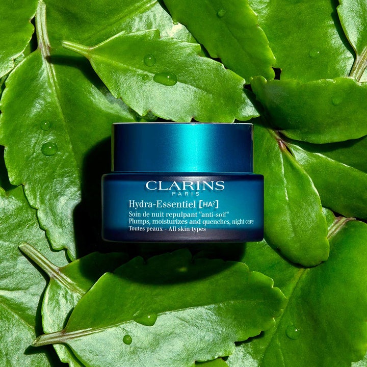 Clarins Hydra-Essentiel nattkräm 50 ml i blå glasburk som vilar på gröna blad med vattendroppar.