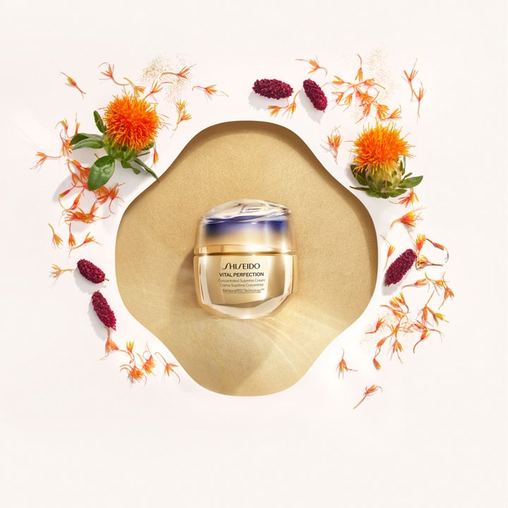 Shiseido Vital Perfection Concentrated Supreme Cream 50 ml lyftande dagkräm i guldburk omgiven av safflorsblommor.