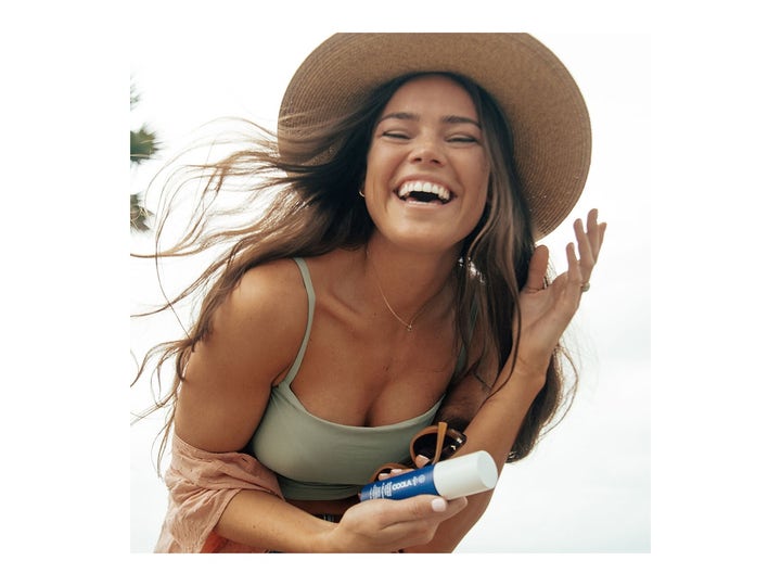 COOLA Refreshing Water Mist SPF15 50 ml solskydd ansikte spray som hålls av en leende kvinna i stråhatt.