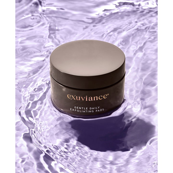 Exuviance Gentle Daily Exfoliating 60 Pads 55 ml daglig exfoliering för glow i svart burk på lila vatten