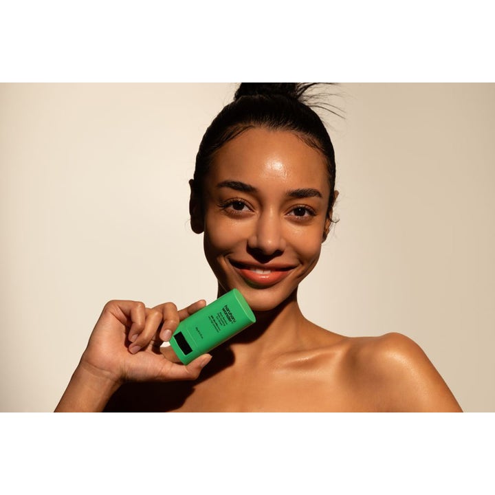 haruharu wonder Black Bamboo Daily Soothing Sun Shield 20 g bärbar solstift i grön hylsa hålls av en kvinna.