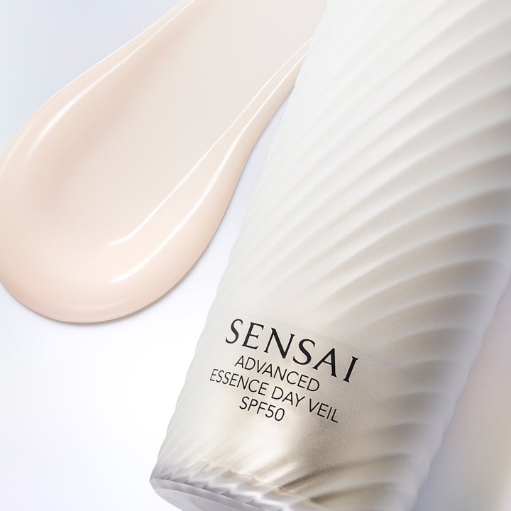 Sensai Advanced Essence Day Veil 40 ml skyddande serum med SPF 50 och krämig textur intill en vit vågformad flaska