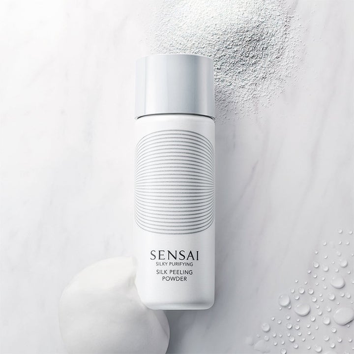 Sensai Silk Peeling Powder ansiktspeeling i vit flaska med finmalt puder och krämigt skum på marmor.