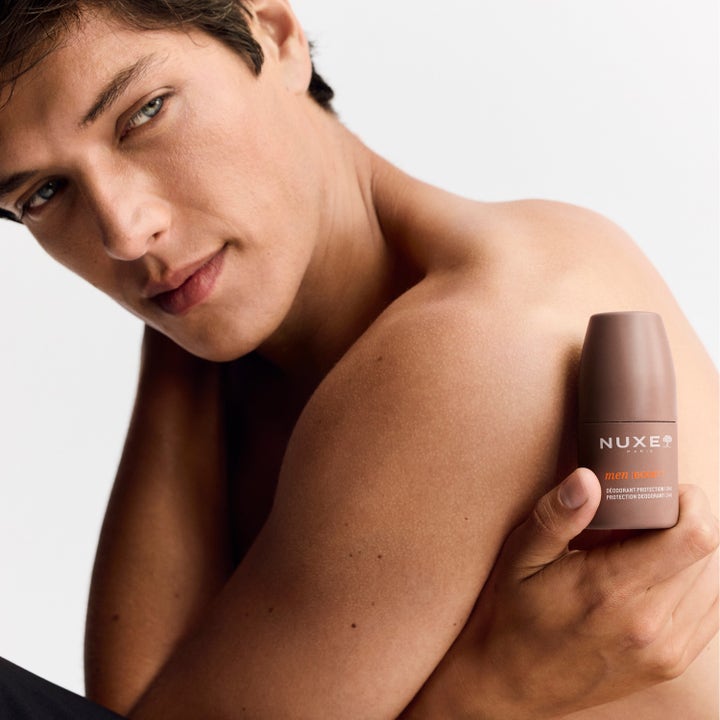 Nuxe Men 24Hr Protect Deo 50 ml i brun roll-on flaska som hålls av en man i en närbild på axeln.