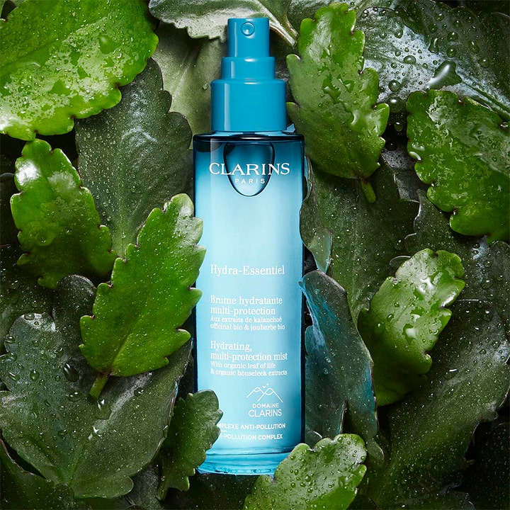 Clarins Hydra-Essentiel 75 ml återfuktande ansiktsmist anti-pollution i blå flaska bland daggvåta gröna blad.