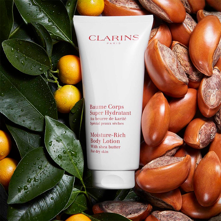 Clarins Moisture-Rich Body Lotion 200 ml återfuktande kroppslotion i vit tub omgiven av sheanötter och gröna blad