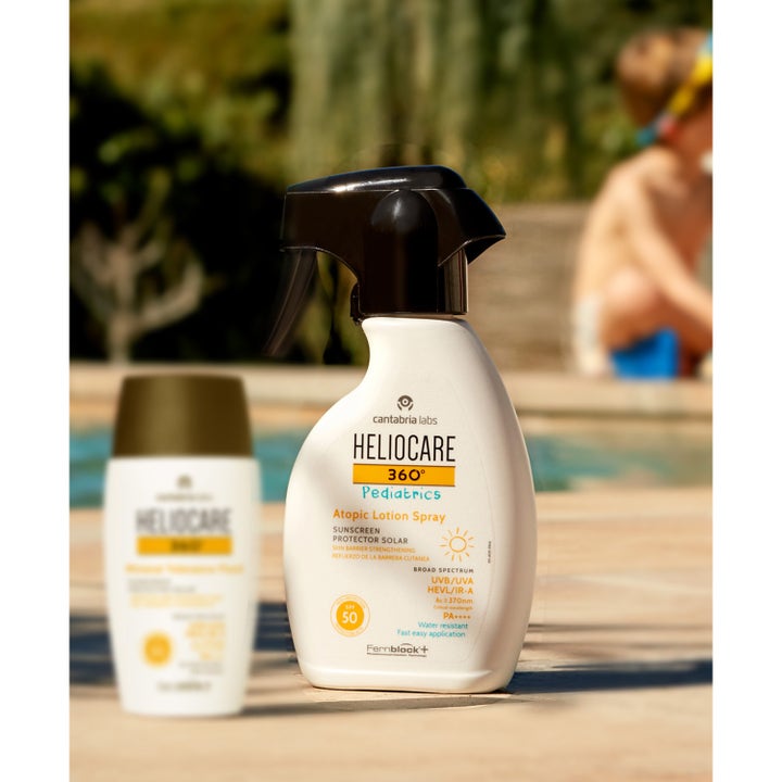 Heliocare Pediatrics Atopic Lotion Spray 250 ml barnsolskydd för atopisk hud i vit flaska med svart trigger vid en pool.