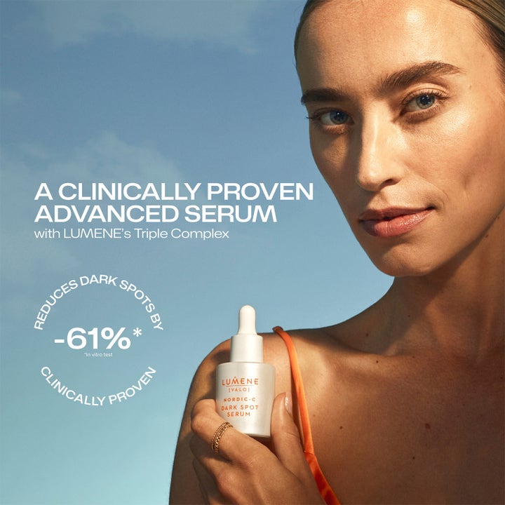 Lumene Dark Spot Serum 30 ml lystergivande ansiktsserum som reducerar mörka fläckar med 61 % hålls av kvinna mot blå himmel.