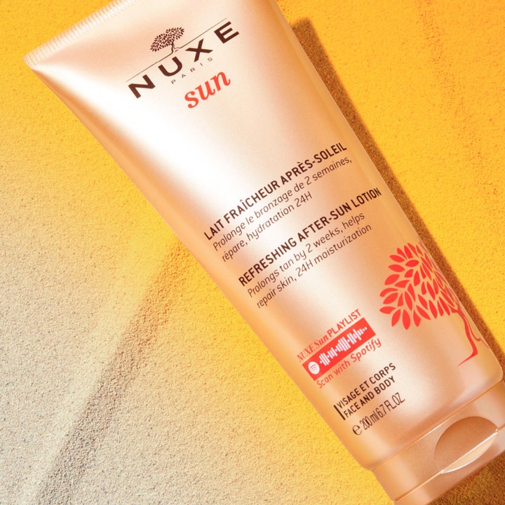 Nuxe Sun Refreshing After Sun Lotion 200 ml i tub på sand som ger 24h hydrating och hjälper till att behålla solbrännan.