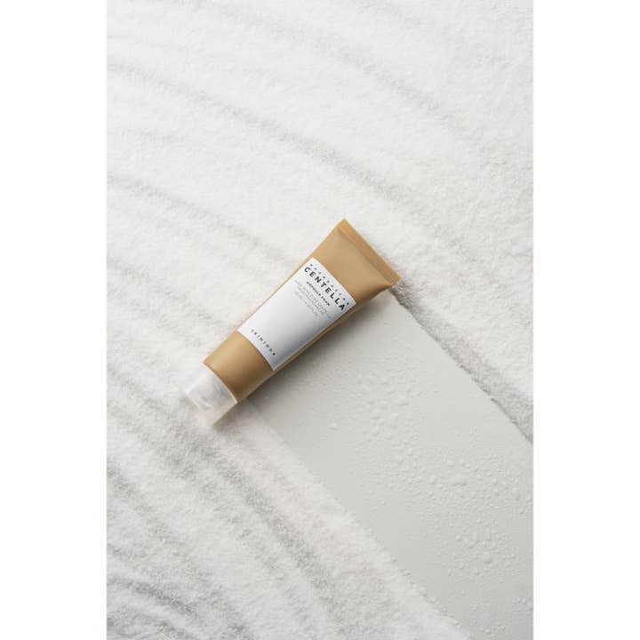 SKIN1004 Madagascar Centella Ampoule Foam 125 ml lugnande ansiktsskum i ljusbrun tub placerad på vit vågig sand