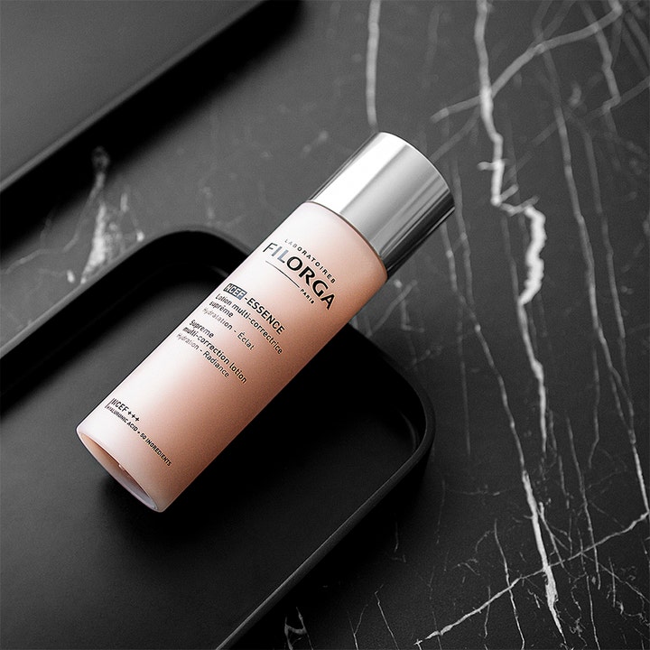 Filorga NCEF-Essence Supreme 150 ml lystergivande essens för ansiktet i rosa flaska med silverlock på svart marmor