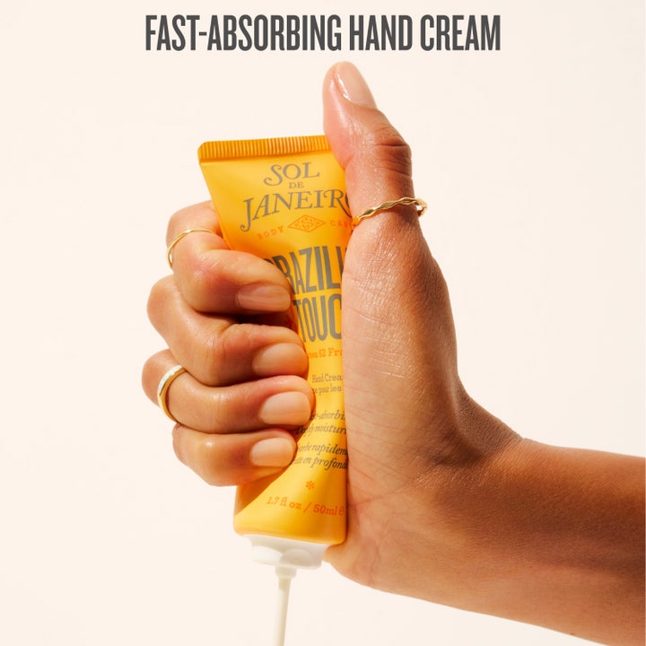 Sol de Janeiro Brazilian Touch Hand Cream 50 ml återfuktande handkräm i gul tub som hålls av händer med olika hudtoner