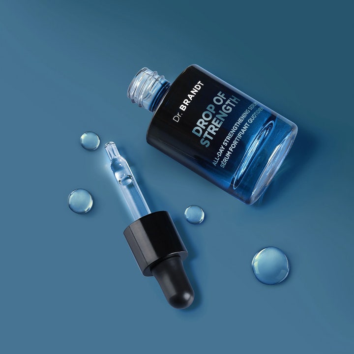 Dr Brandt Drop Of Strength 30 ml stärkande serum i mörk glasflaska med pipett och klara droppar på blå yta